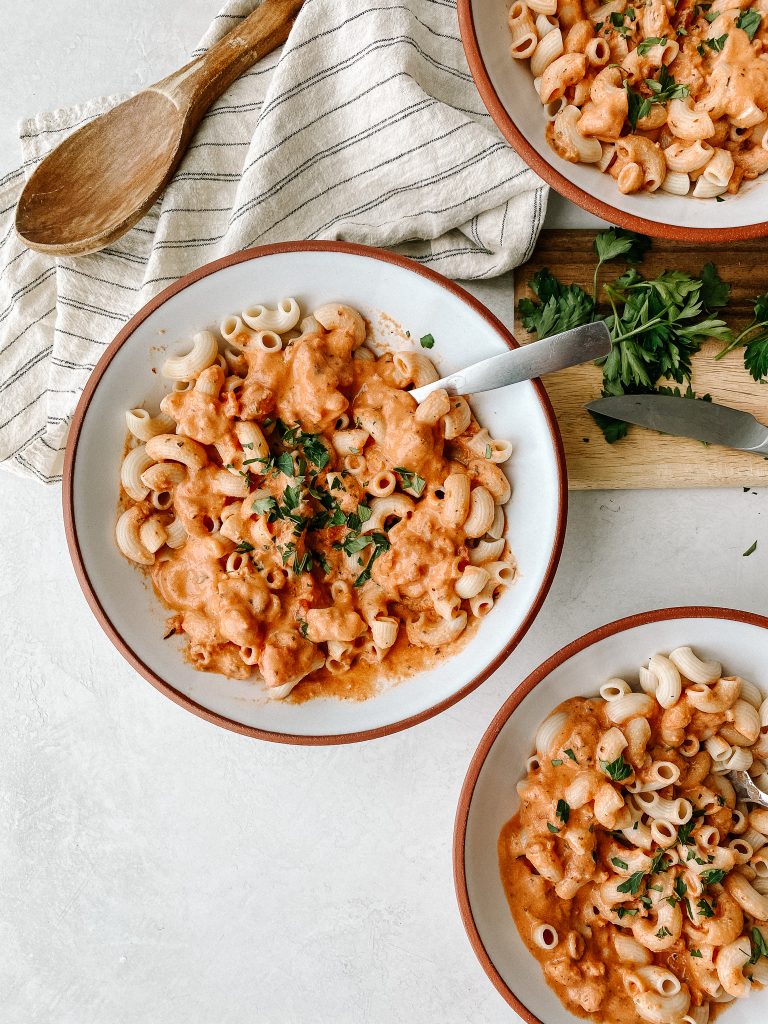 dairy free creamy tomato pasta in bowls with parsley on a cutting board and a dish towel
