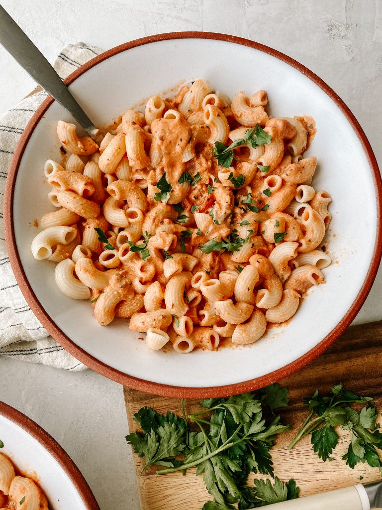 dairy free creamy tomato pasta in a bowl with parsley on a cutting board 