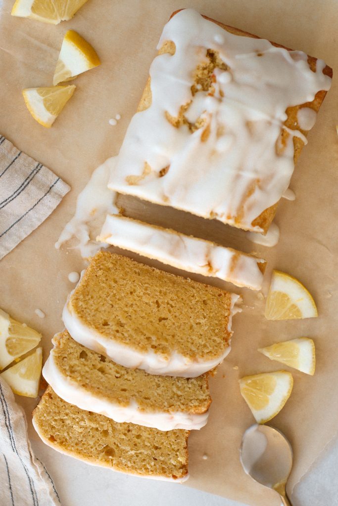 Gluten free lemon loaf with lemon glaze on parchment paper with slices of lemon
