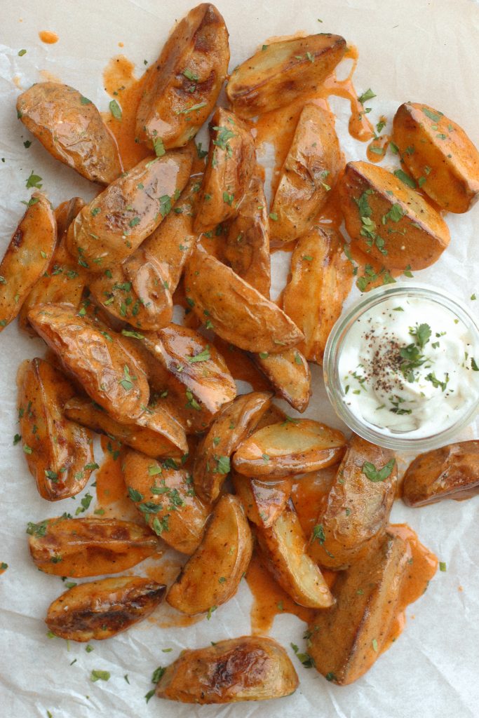 potato wedges with buffalo sauce on parchment paper with bowl of ranch