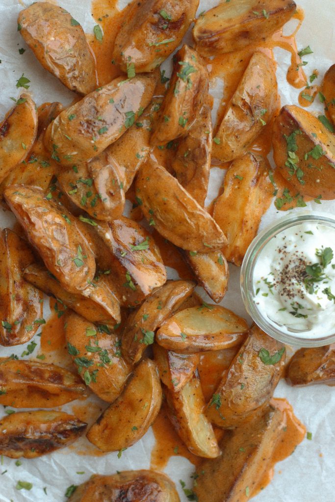 potato wedges with buffalo sauce on parchment paper with bowl of ranch