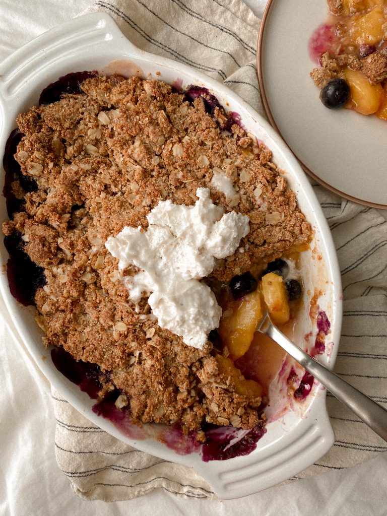 peach and blueberry crisp with a spoon in a baking dish with cool whip on top