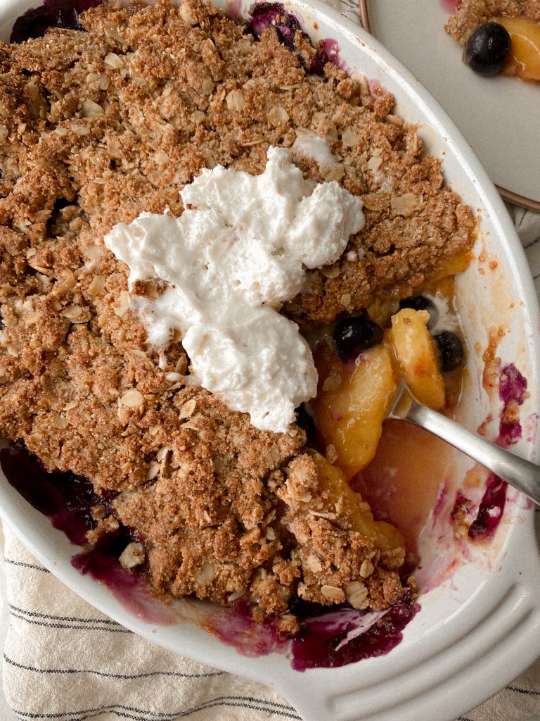 peach and blueberry crisp with a spoon in a baking dish with cool whip on top