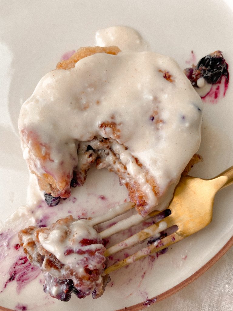 blueberry cinnamon roll on a plate with a gold fork with bite
