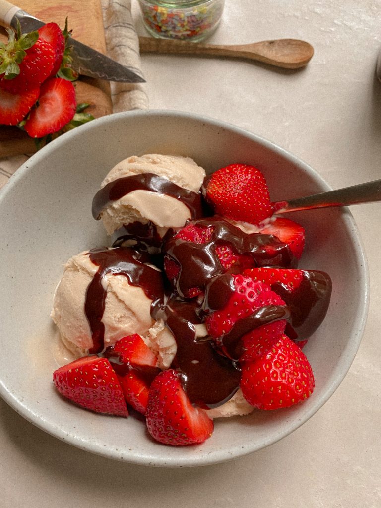 vanilla ice cream in a white bowl with strawberries and hot fudge