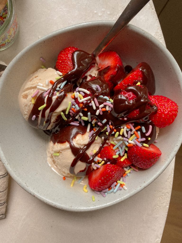 vanilla ice cream in a white bowl with strawberries and hot fudge and sprinkles