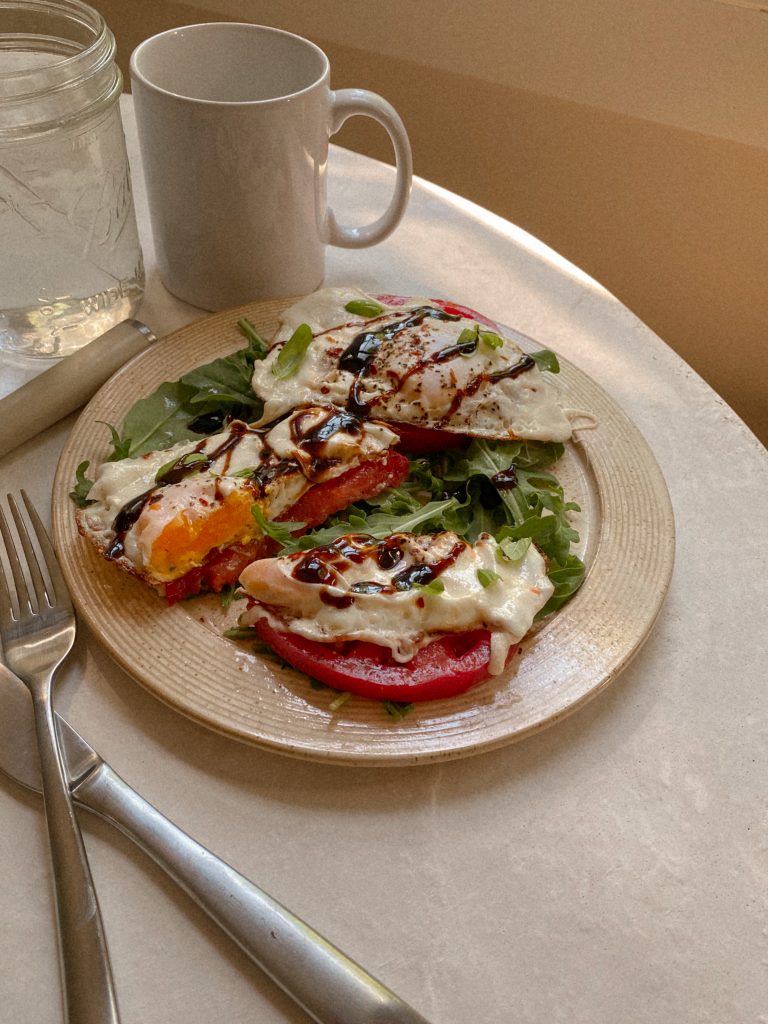 caprese eggs on a plate with white mug and jar of water with glass straw on table