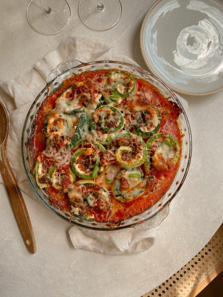 zucchini lasagna roll ups in a glass baking dish on table with white towel and wooden spoon