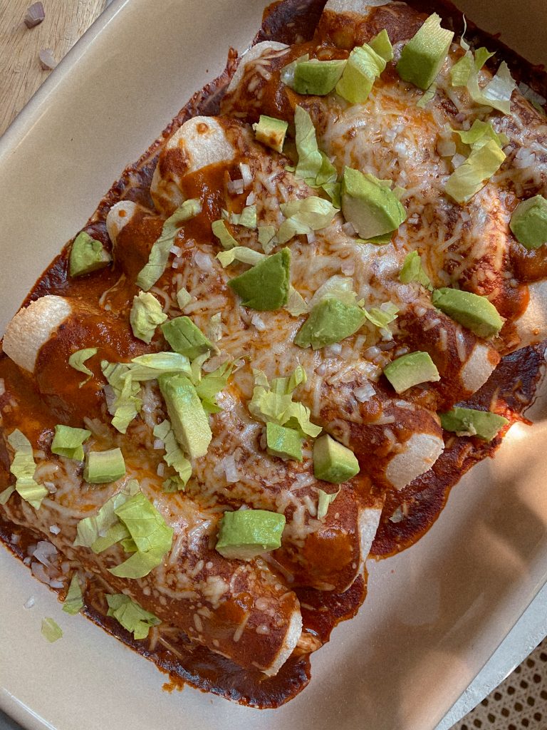 enchiladas in a baking dish with avocado slices and lettuce