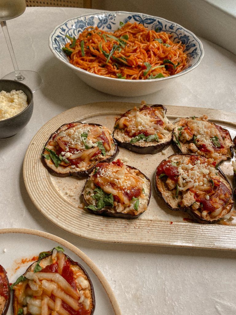 eggplant pizzas on a dish with a bowl of spaghetti and small bowl of parmesan