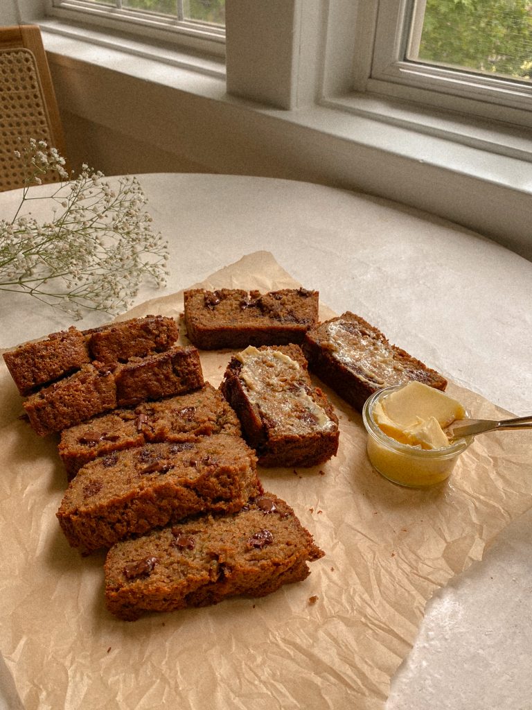 zucchini bread slices on brown parchment paper with small bowl of butter and white flowers