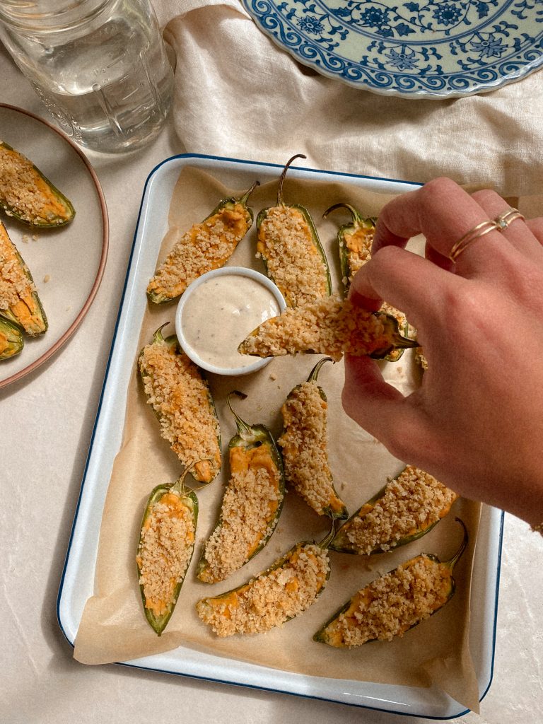hand dipping jalapeno popper in ranch with tray of jalapeno poppers