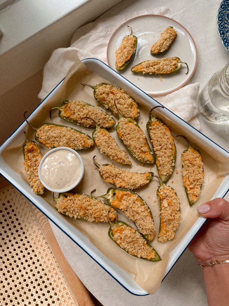 hand holding tray of jalapeno poopers with small bowl of ranch on parchmenet paper