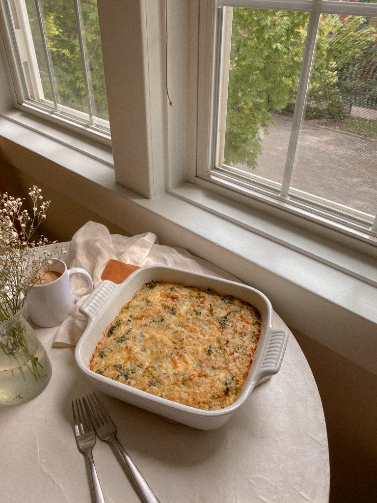 quinoa breakfast bake in a white baking dish with wood spoon and cup of coffee on a table with window