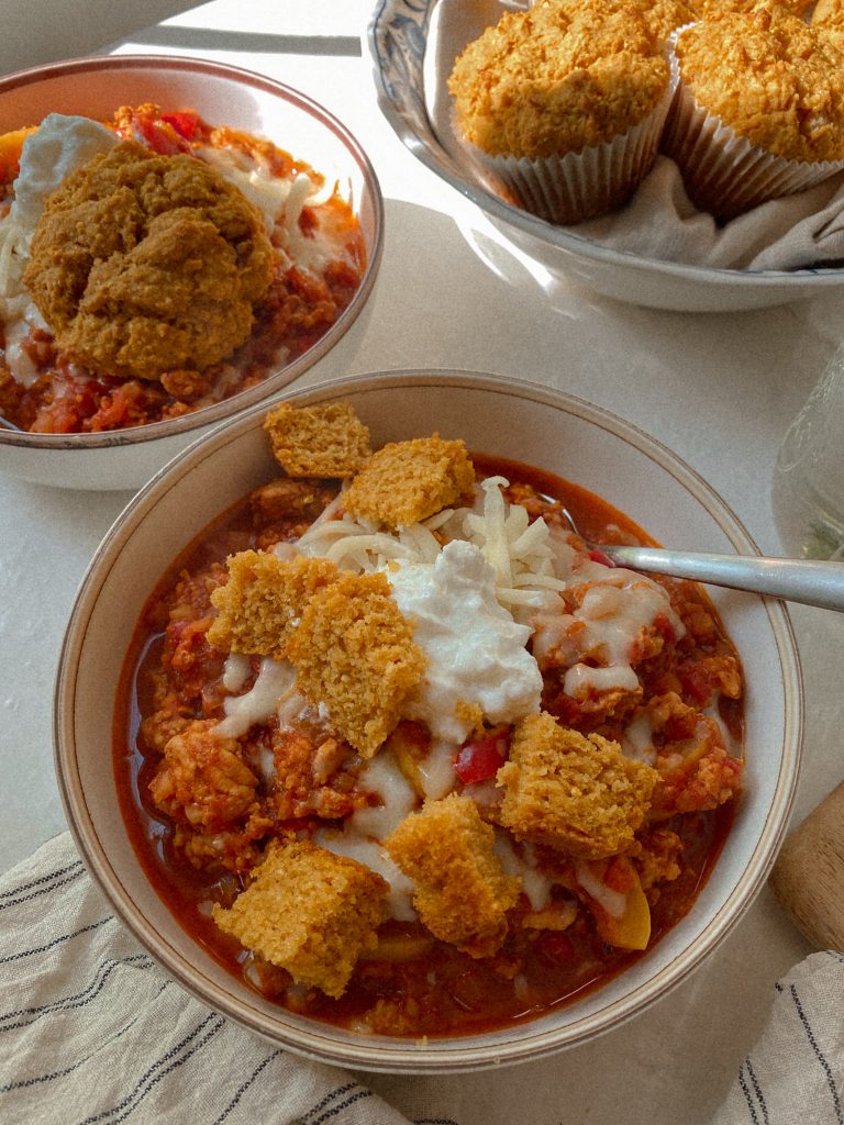 chicken chili in a bowl with cheese and sour cream and cubes of cornbread