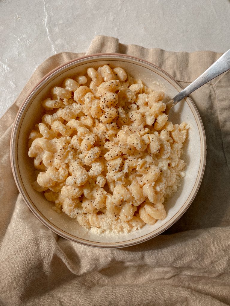 creamy cavatappi pasta in a white bowl with a dish towel