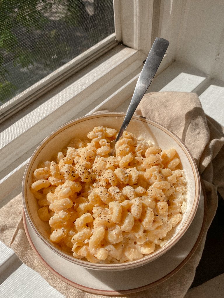 creamy cavatappi pasta in a white bowl with a dish towel on a window sill
