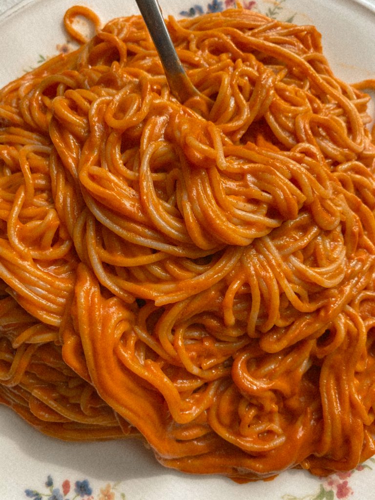 creamy vegan spaghetti on a white floral plate with a fork