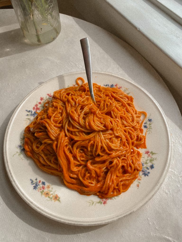 creamy vegan spaghetti on a white floral plate with a fork
