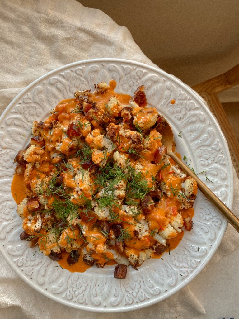 cauliflower with harissa tahini sauce, dates, and fresh dill on a white plate with a gold spoon