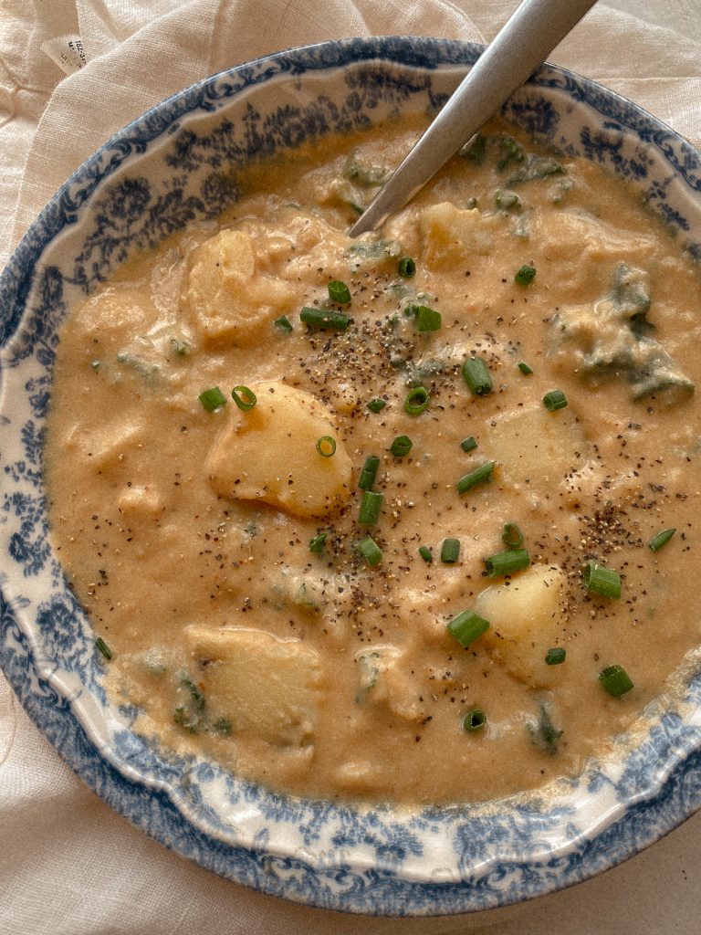creamy vegan potato soup with chives in a blue and white bowl with a spoon