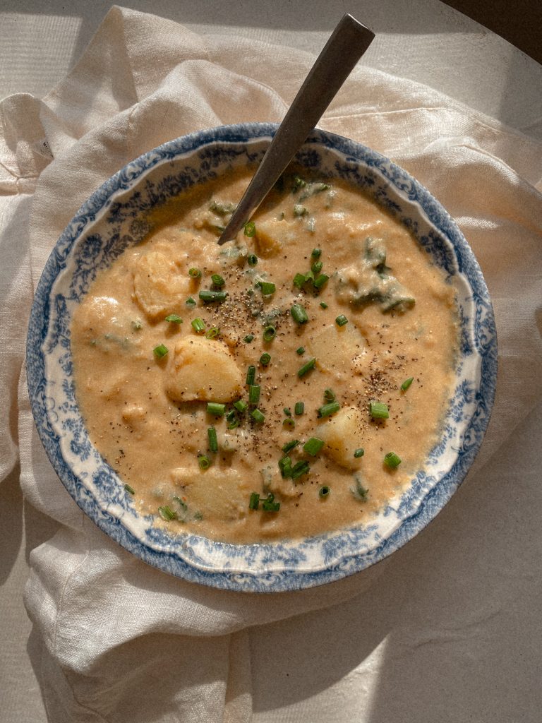creamy vegan potato soup with chives in a blue and white bowl with a spoon