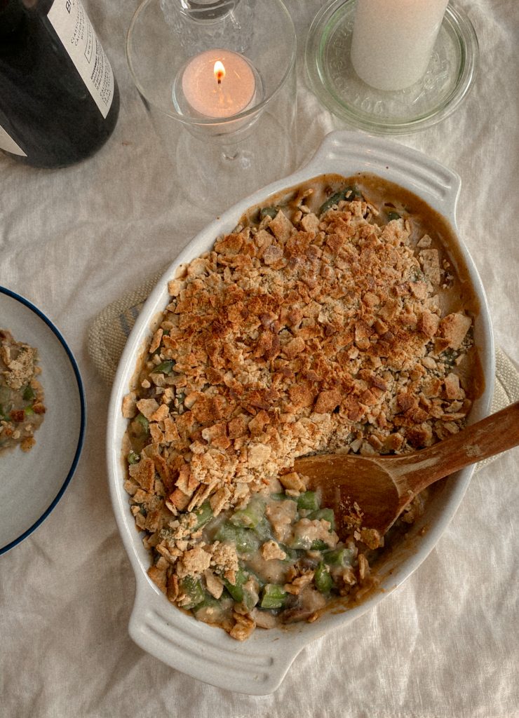 green bean casserole in a white baking dish with wood spoon and candles and bottle of wine on table 