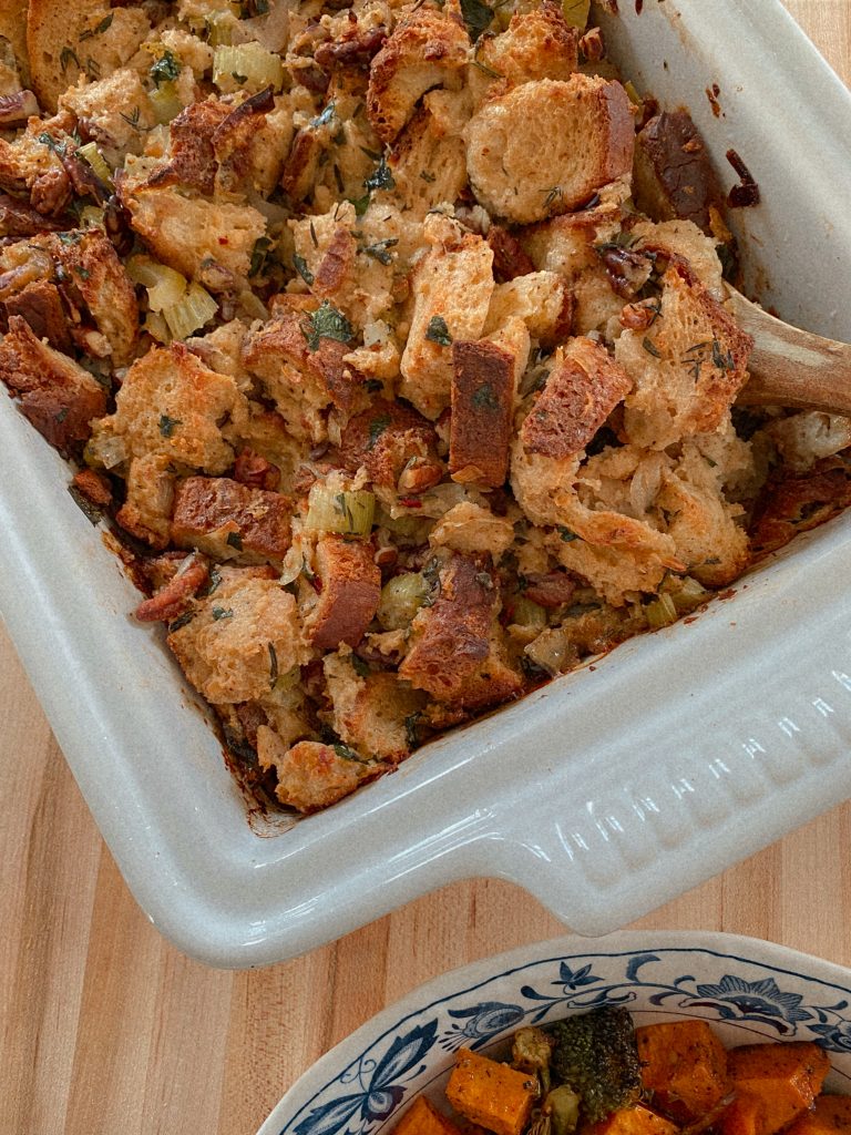 stuffing in a white baking dish with a wooden spoon and a bowl of sweet potatoes