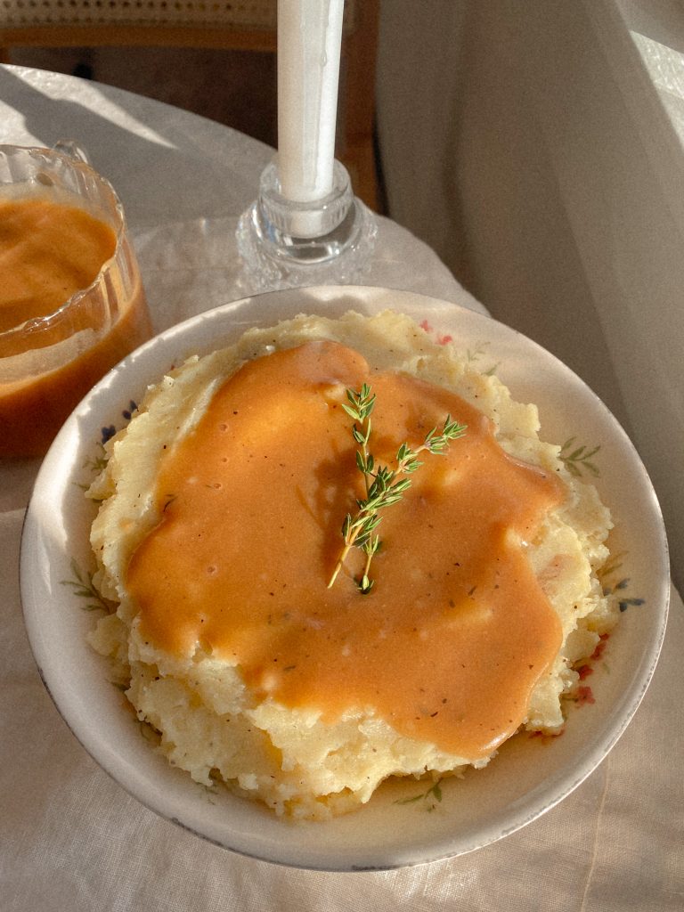 mashed potatoes and gravy with 2 sprigs of thyme in a white bowl with a small bowl of gravy