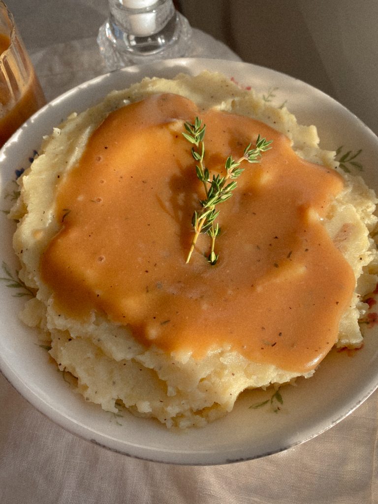mashed potatoes and gravy with 2 sprigs of thyme in a white bowl