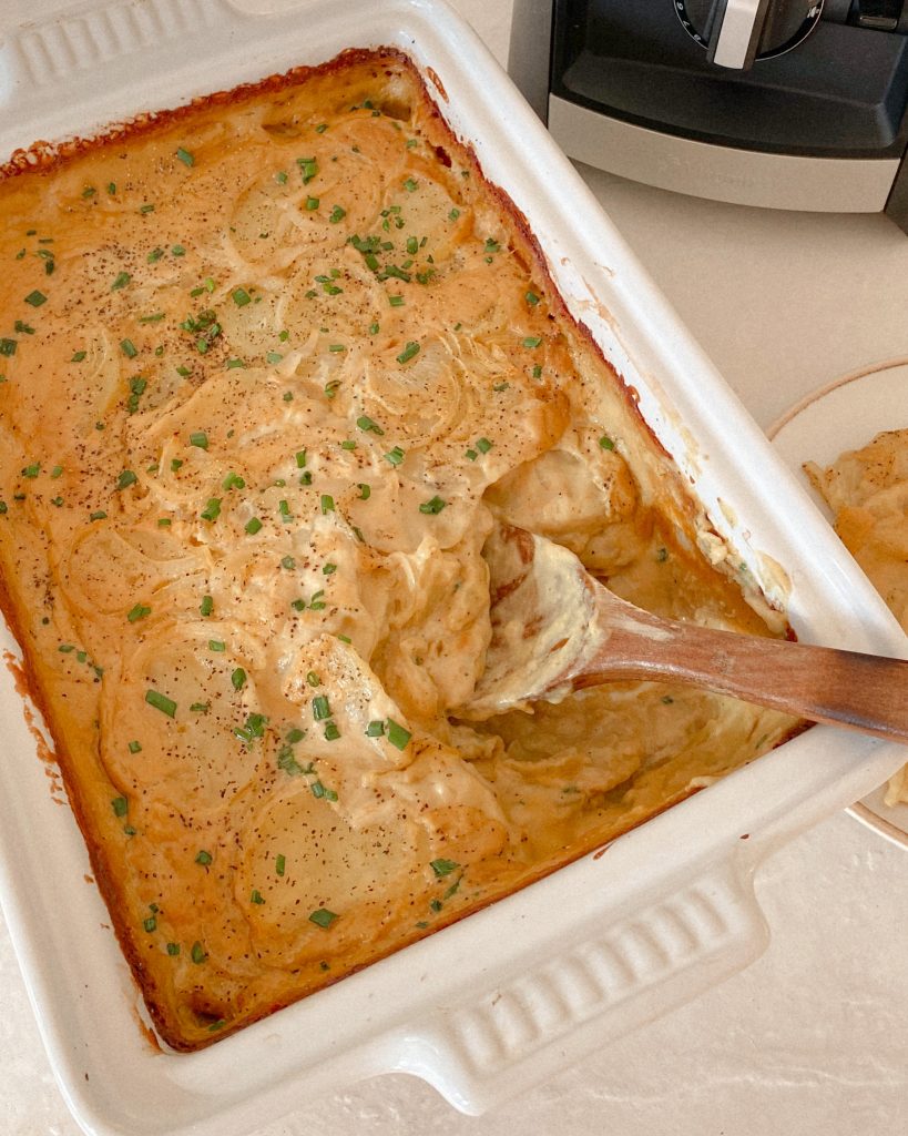 vegan cheesy scalloped potatoes in a white casserole dish with a wooden spoon