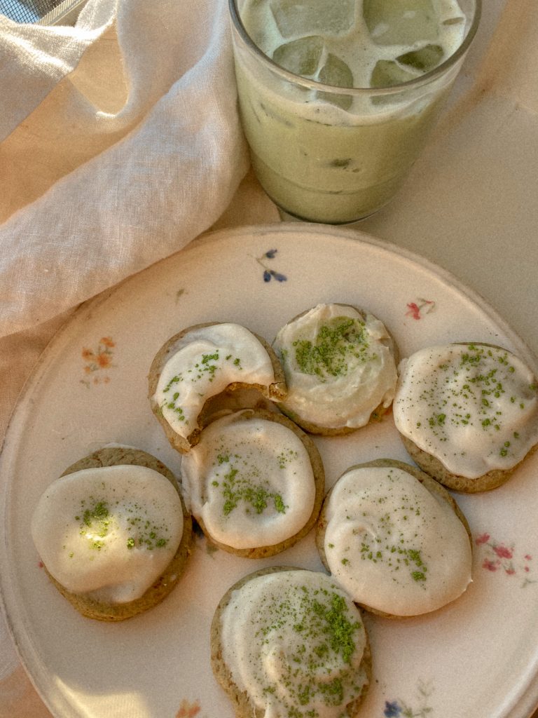 matcha cookies with vanilla frosting on a floral plate with a glass of iced matcha tea