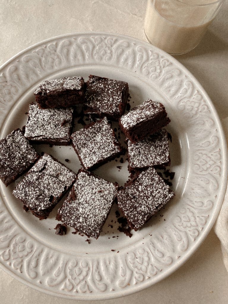 brownies with powdered sugar on a white plate with a glass of milk