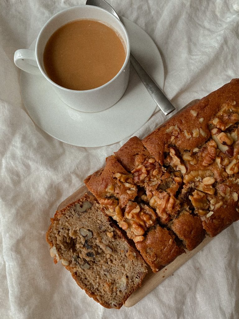 walnut banana bread sliced on a wood board with white mug of coffee