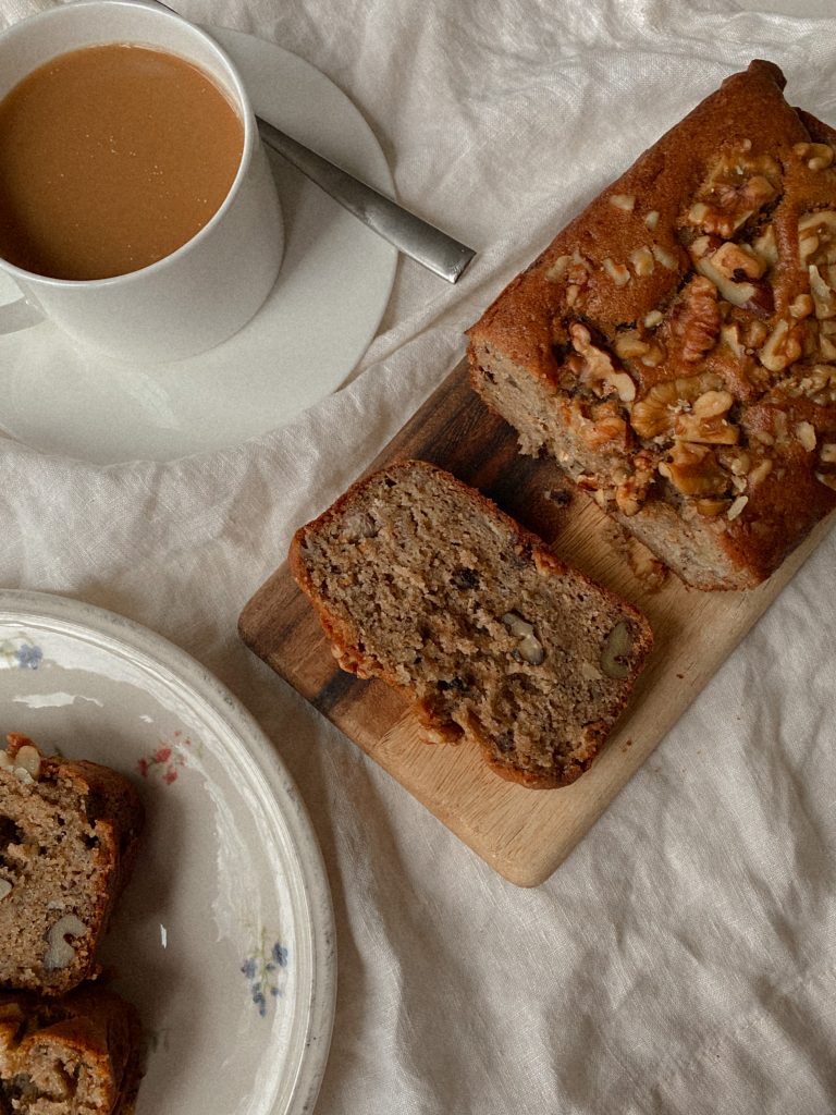 walnut banana bread sliced on a wood board with white mug of coffee and slices on a plate