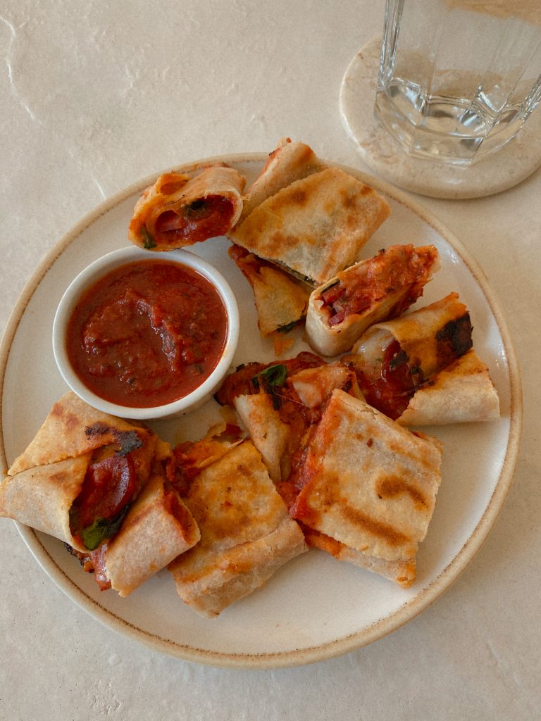 pizza rolls on a white plate with small bowl of pizza sauce and a glass of water