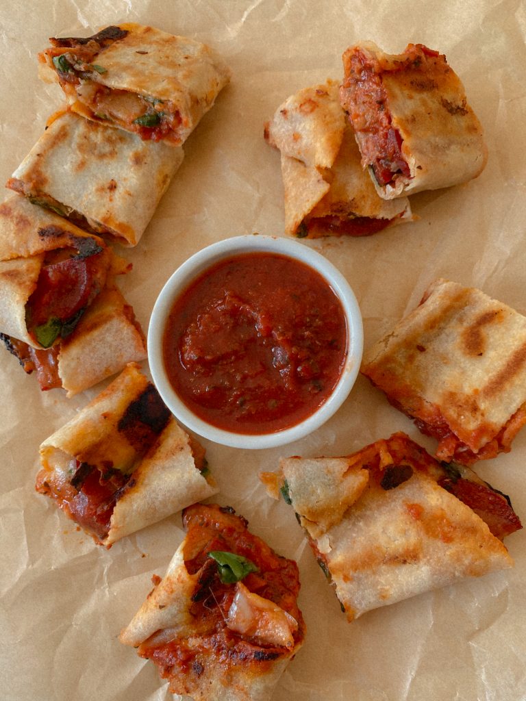 pizza rolls on brown parchment paper with small bowl of pizza sauce