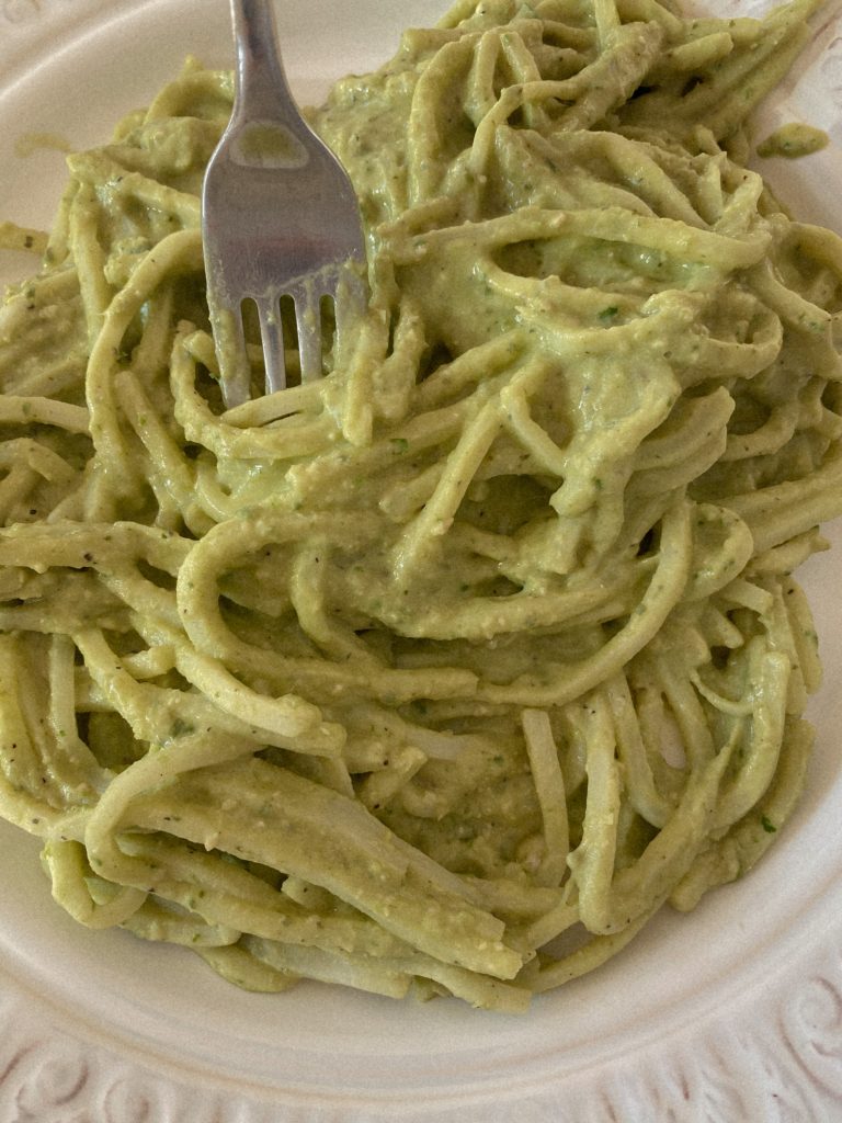 creamy pesto pasta on a white plate with a fork