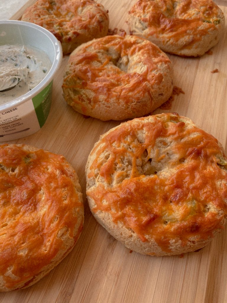 jalapeno cheddar bagels on a wood cutting board with a container of chive cream cheese