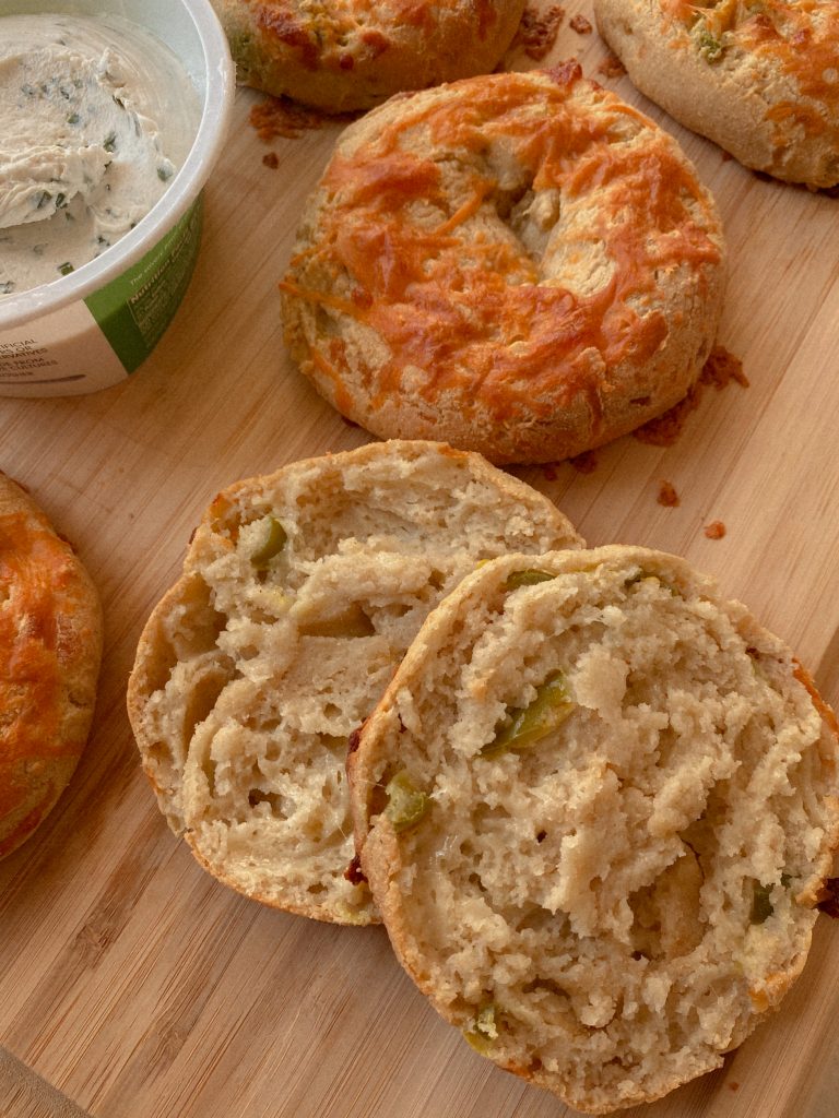 jalapeno cheddar bagels on a wood cutting board with 1 sliced open with a container of chive cream cheese