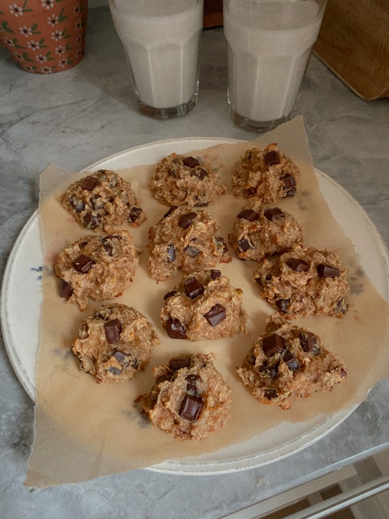banana coconut chocolate chip cookies on a plate with parchment paper with 2 glasses of milk
