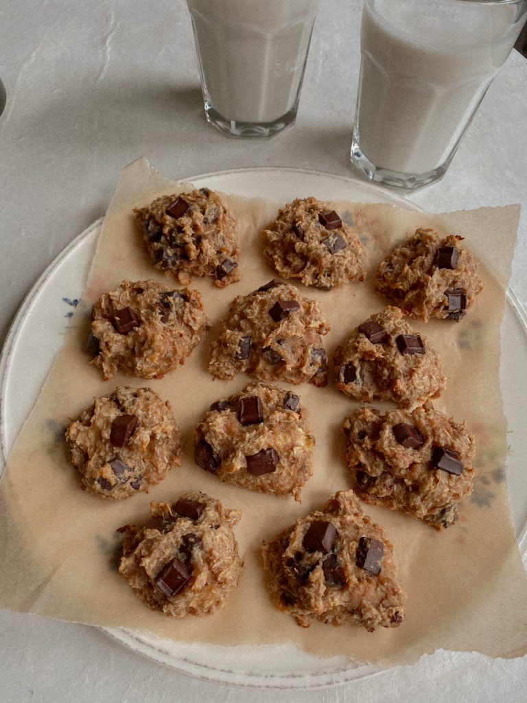 banana coconut chocolate chip cookies on a plate with parchment paper with 2 glasses of milk