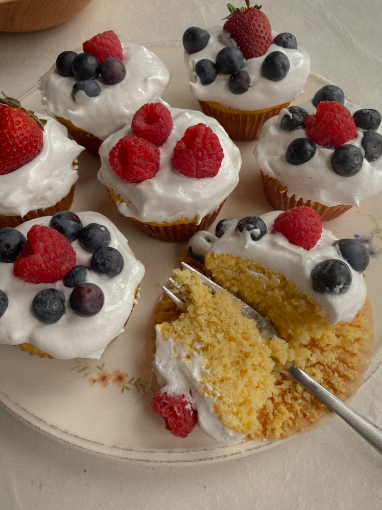 cupcakes with cool whip frosting and berries on top on a white plate with one cupcake sliced open