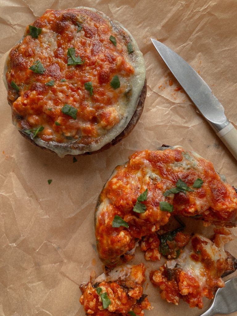two portobello pizzas on brown parchment paper with a knife
