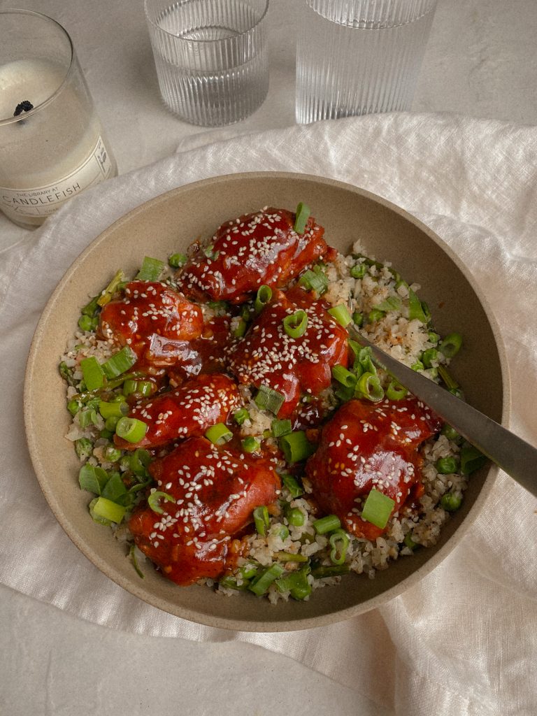honey sesame chicken and cauliflower rice with green onions in a bowl with a spoon