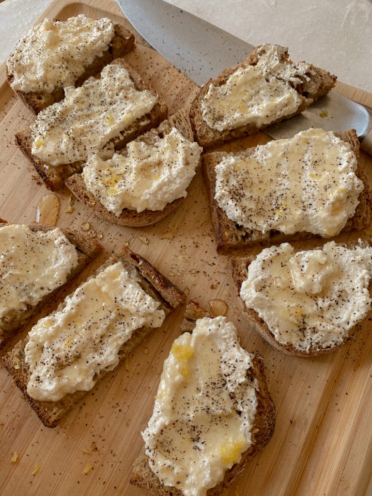 lemon ricotta toasts with honey and black pepper sliced on a wood cutting board 