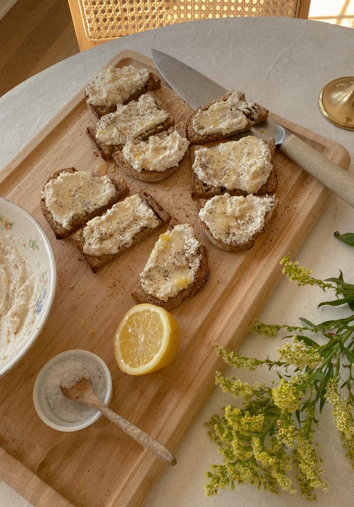 lemon ricotta toasts sliced on a wood cutting board with small bowl of salt with a wood spoon and a lemon with yellow flowers