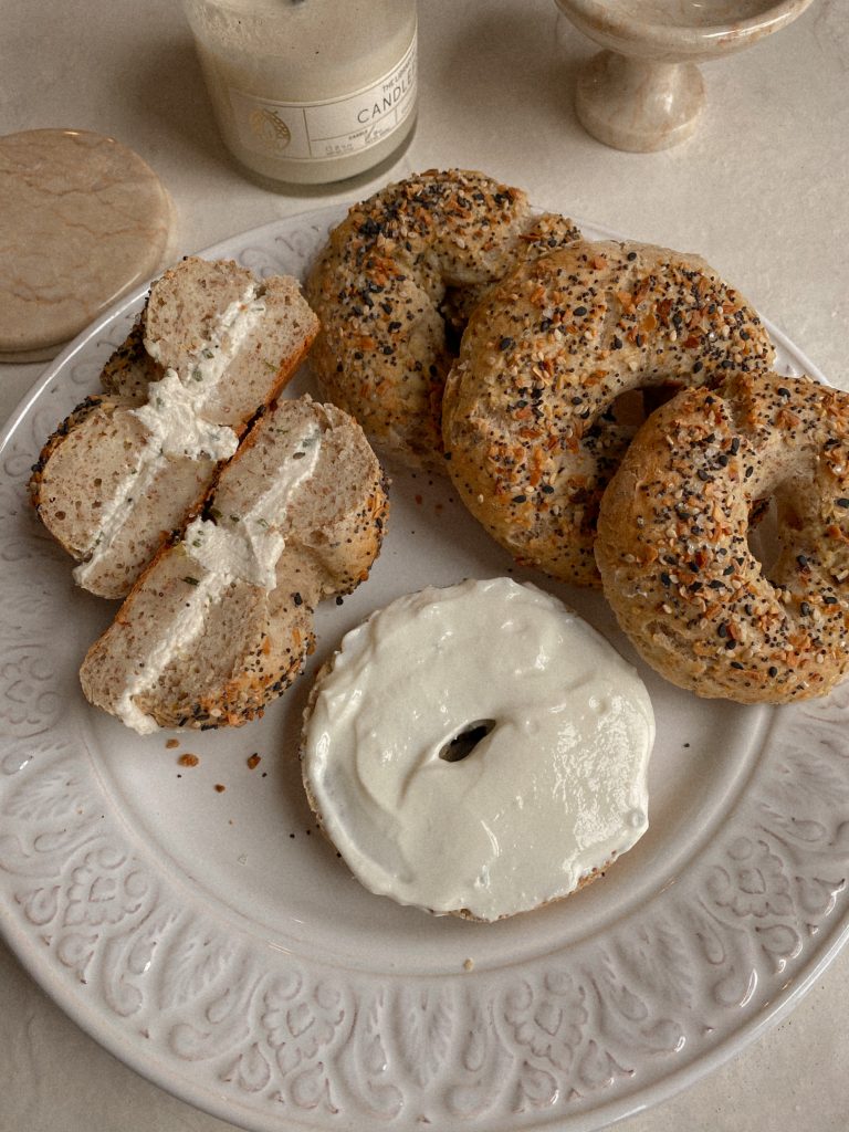bagels on a white plate with cream cheese with a white candle and marble coasters