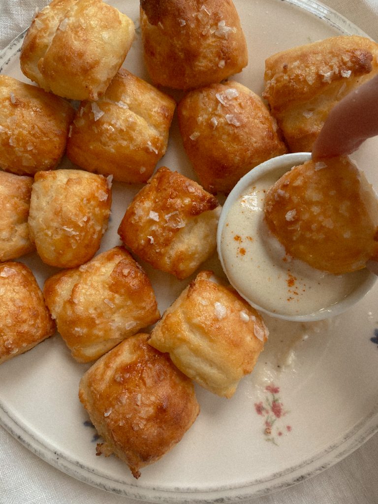 close up of gluten-free pretzel bites being dipped into cheese sauce with flaky salt 