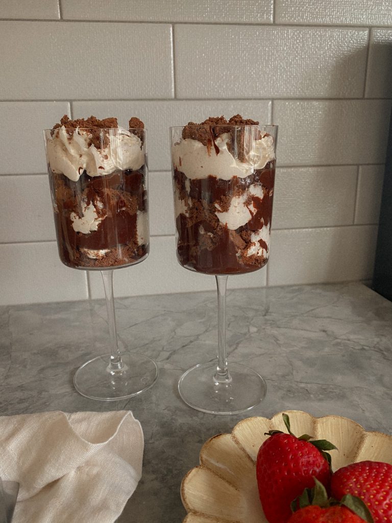 Vegan and Paleo Avocado Chocolate Pudding layered in a Wine Glass with coconut cool whip and gluten-free chocolate cookie crumbles 